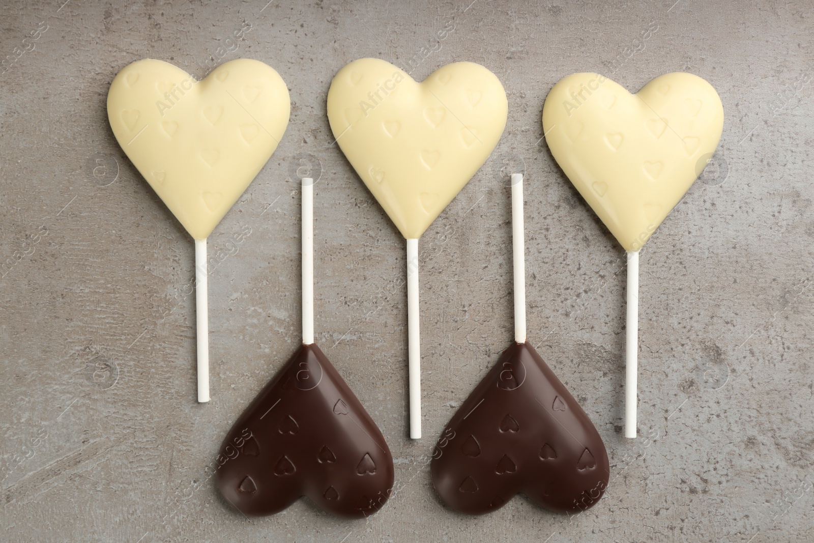 Photo of Different chocolate heart shaped lollipops on grey table, flat lay