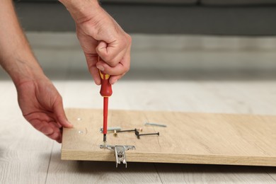Photo of Man with screwdriver assembling furniture on floor indoors, closeup. Space for text