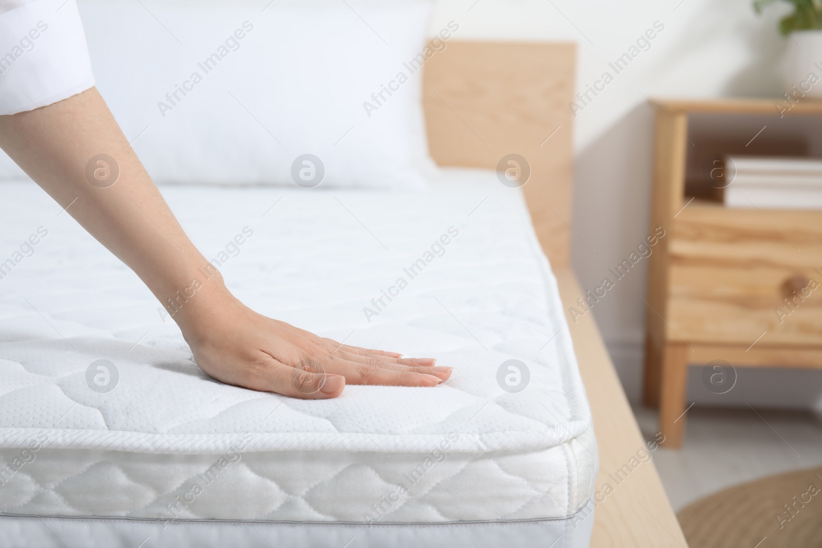 Photo of Woman touching soft white mattress on bed indoors, closeup