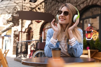 Happy young woman with coffee and headphones listening to music in outdoor cafe