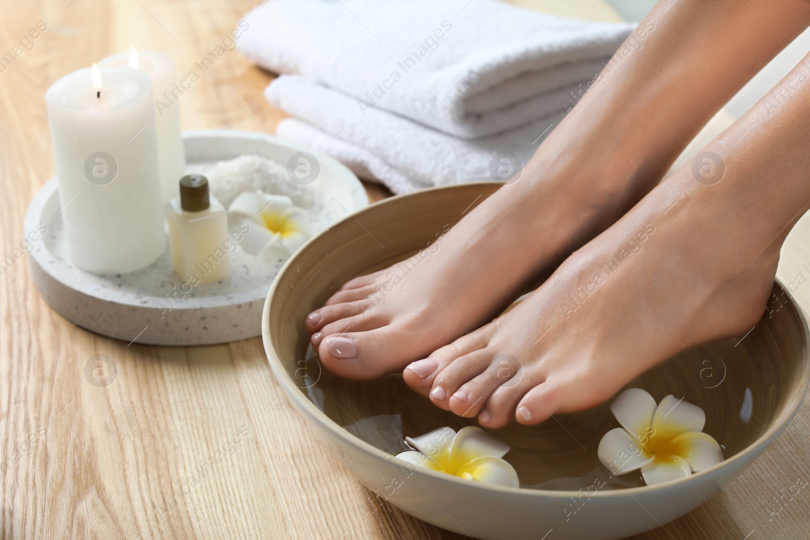 Photo of Closeup view of woman soaking her feet in dish with water and flowers on wooden floor. Spa treatment