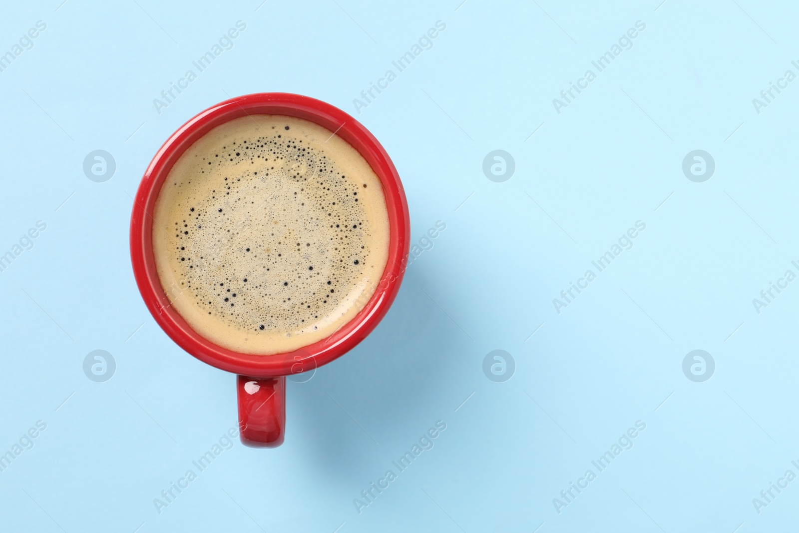 Photo of Tasty coffee in cup on light blue background, top view. Space for text