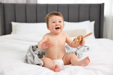 Happy baby boy with blanket and rattle sitting on bed at home