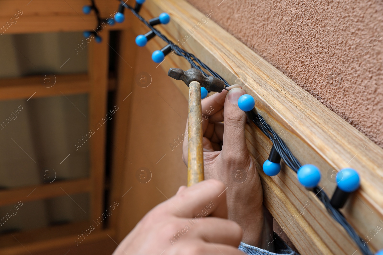 Photo of Man decorating house with Christmas lights outdoors, closeup