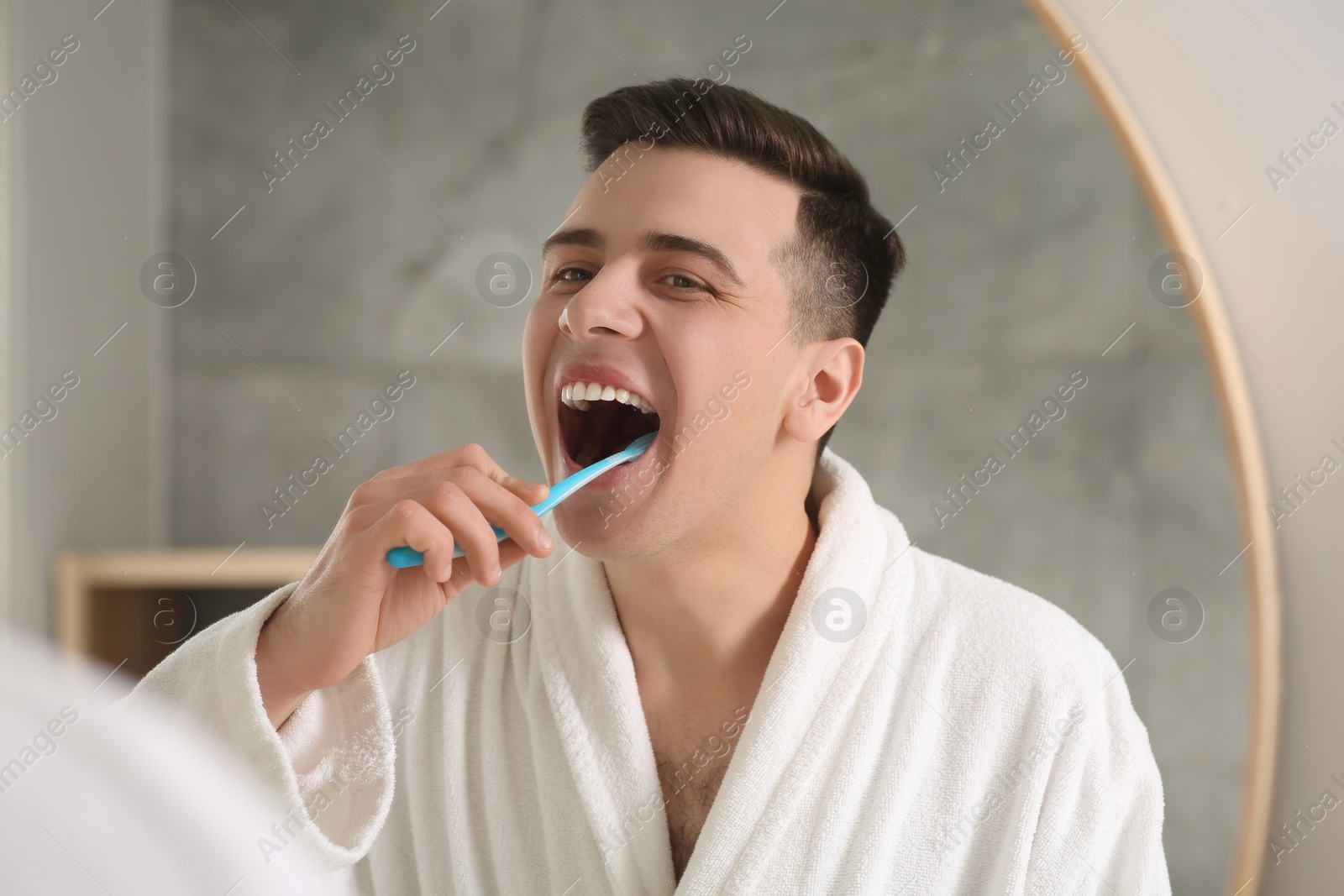 Photo of Man brushing his teeth with toothbrush near mirror in bathroom