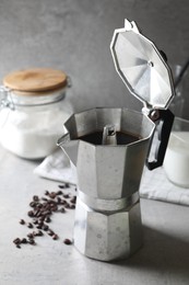 Brewed coffee in moka pot and beans on light grey table