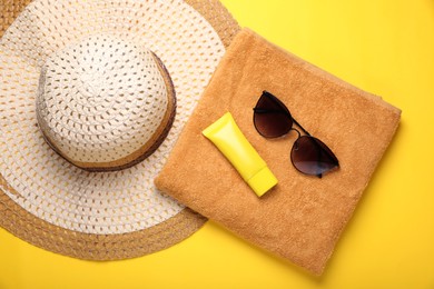 Photo of Straw hat, stylish sunglasses, towel and sunscreen on yellow background, flat lay. Beach accessories