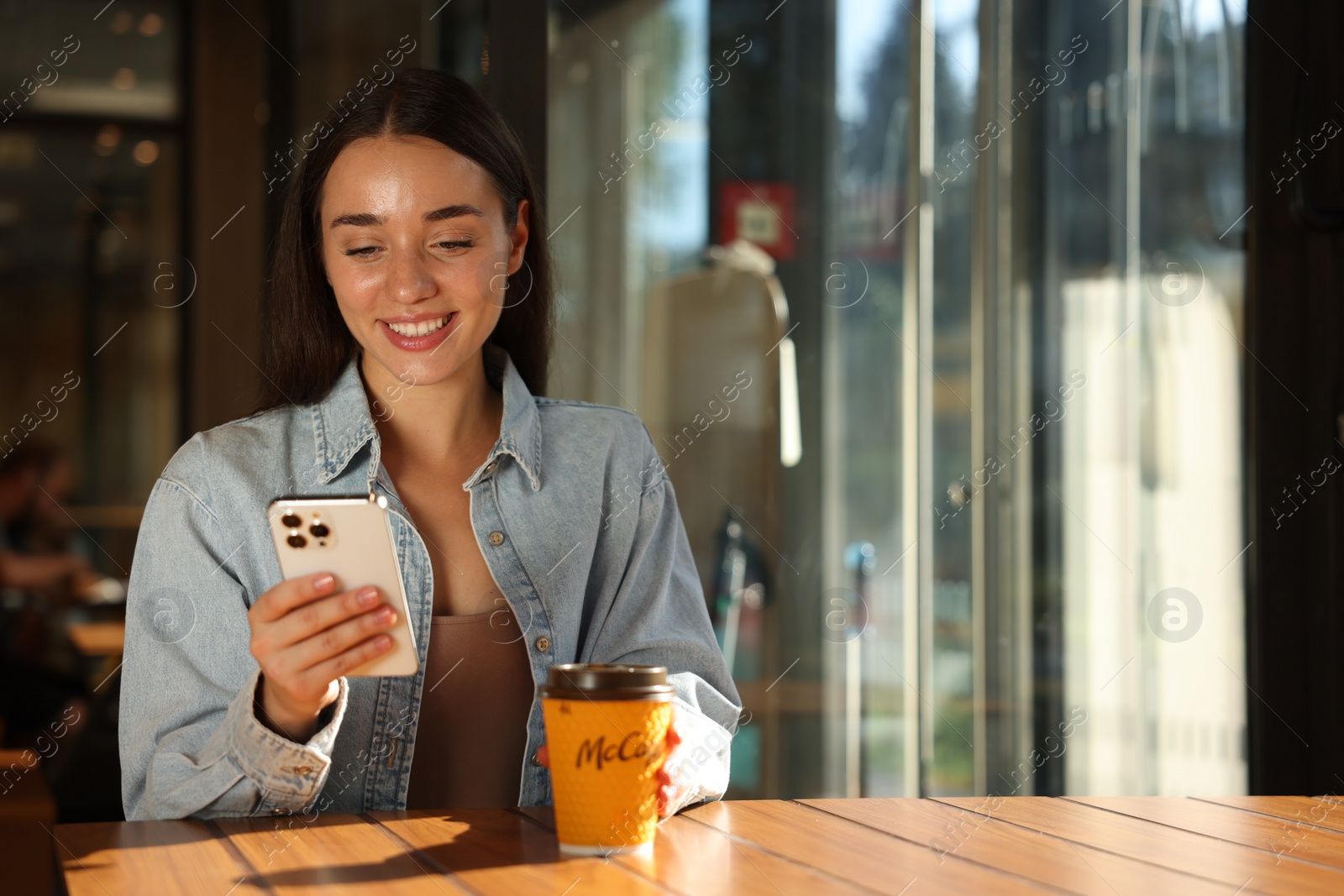 Photo of Lviv, Ukraine - September 26, 2023: Woman with hot McDonald's drink and smartphone at table in cafe, space for text