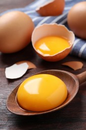 Spoon with raw egg yolk on wooden table, closeup