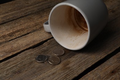 Photo of Poverty. Overturned dirty cup and coins on wooden table, closeup. Space for text