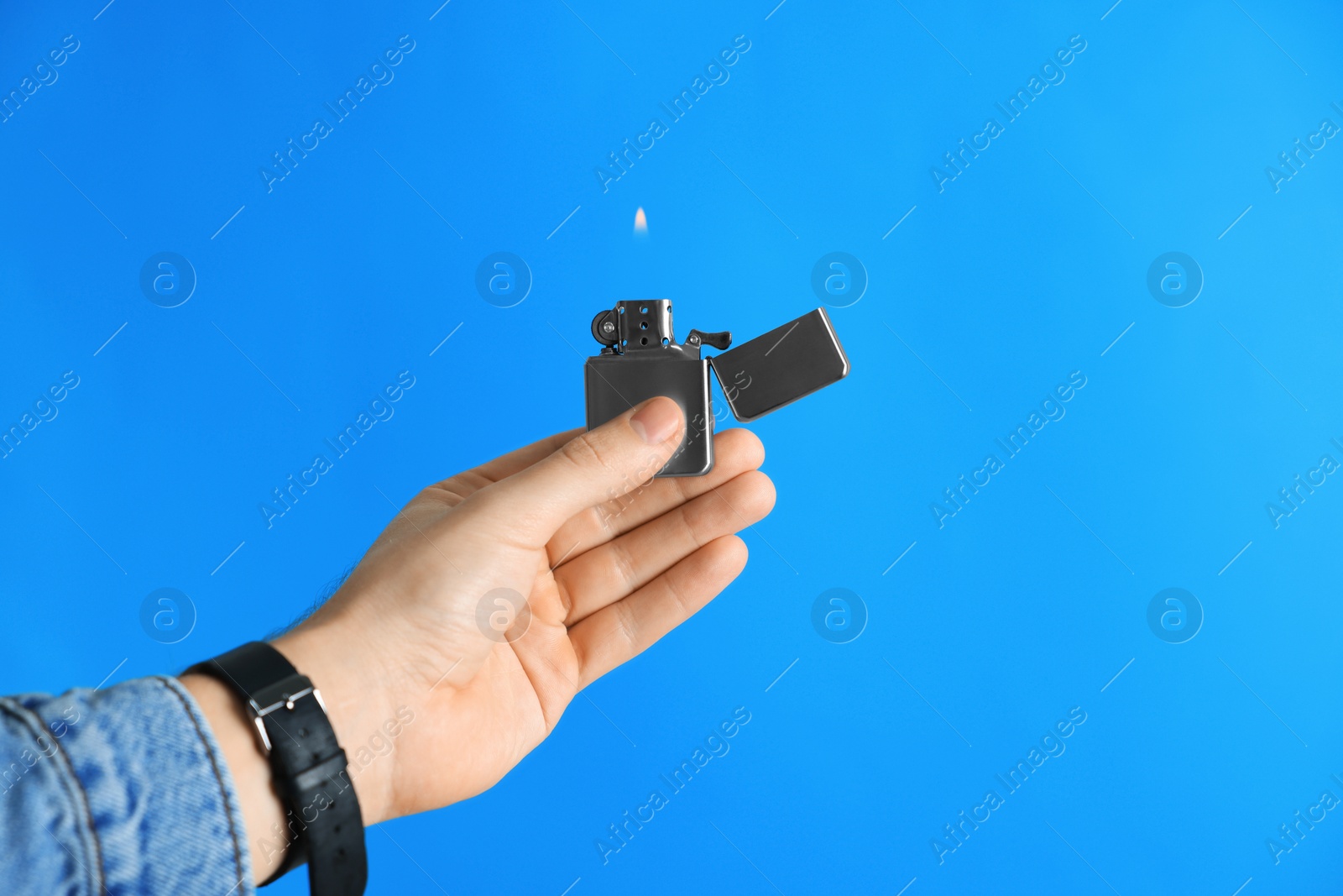 Photo of Man holding lighter with burning flame on light blue background, closeup. Space for text