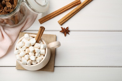 Photo of Cup of hot drink with marshmallows and aromatic cinnamon on white wooden table, flat lay. Space for text