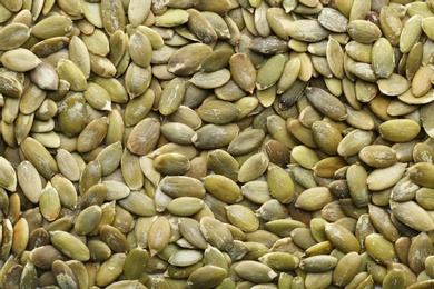 Photo of Shelled raw pumpkin seeds as background, top view