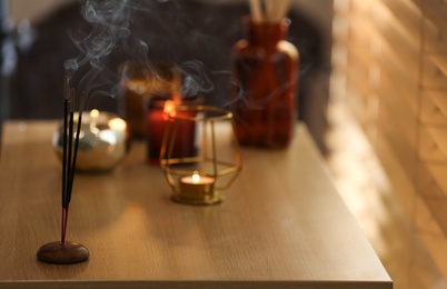 Photo of Incense sticks smoldering on wooden table near window in room. Space for text