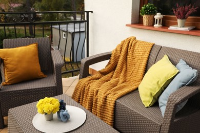 Photo of Colorful pillows, soft blanket and yellow chrysanthemum flowers on rattan garden furniture outdoors