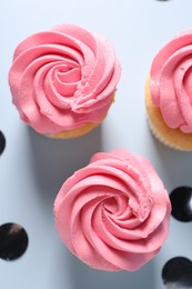 Delicious cupcakes with bright cream and confetti on light background, flat lay