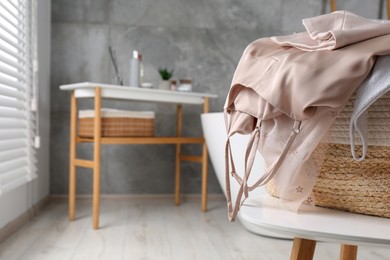 Wicker laundry basket with clothes on stool in bathroom, closeup