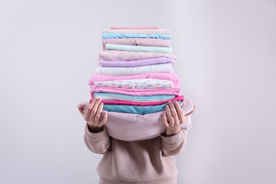 Woman holding stack of clean bed linens on light background