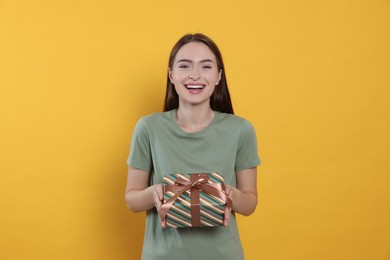 Photo of Portrait of emotional young woman with gift box on yellow background