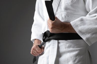 Photo of Karate coach wearing kimono and black belt on grey background, closeup. Space for text