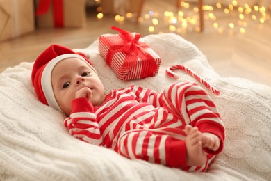 Photo of Cute little baby wearing Santa hat on blanket in room with Christmas lights