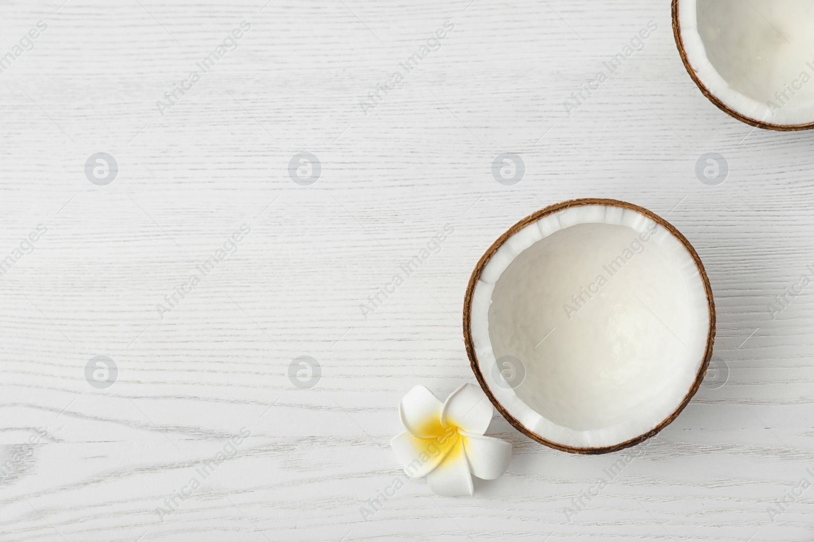 Photo of Halves of coconut and flower on white wooden background, top view. Space for text