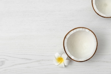 Halves of coconut and flower on white wooden background, top view. Space for text