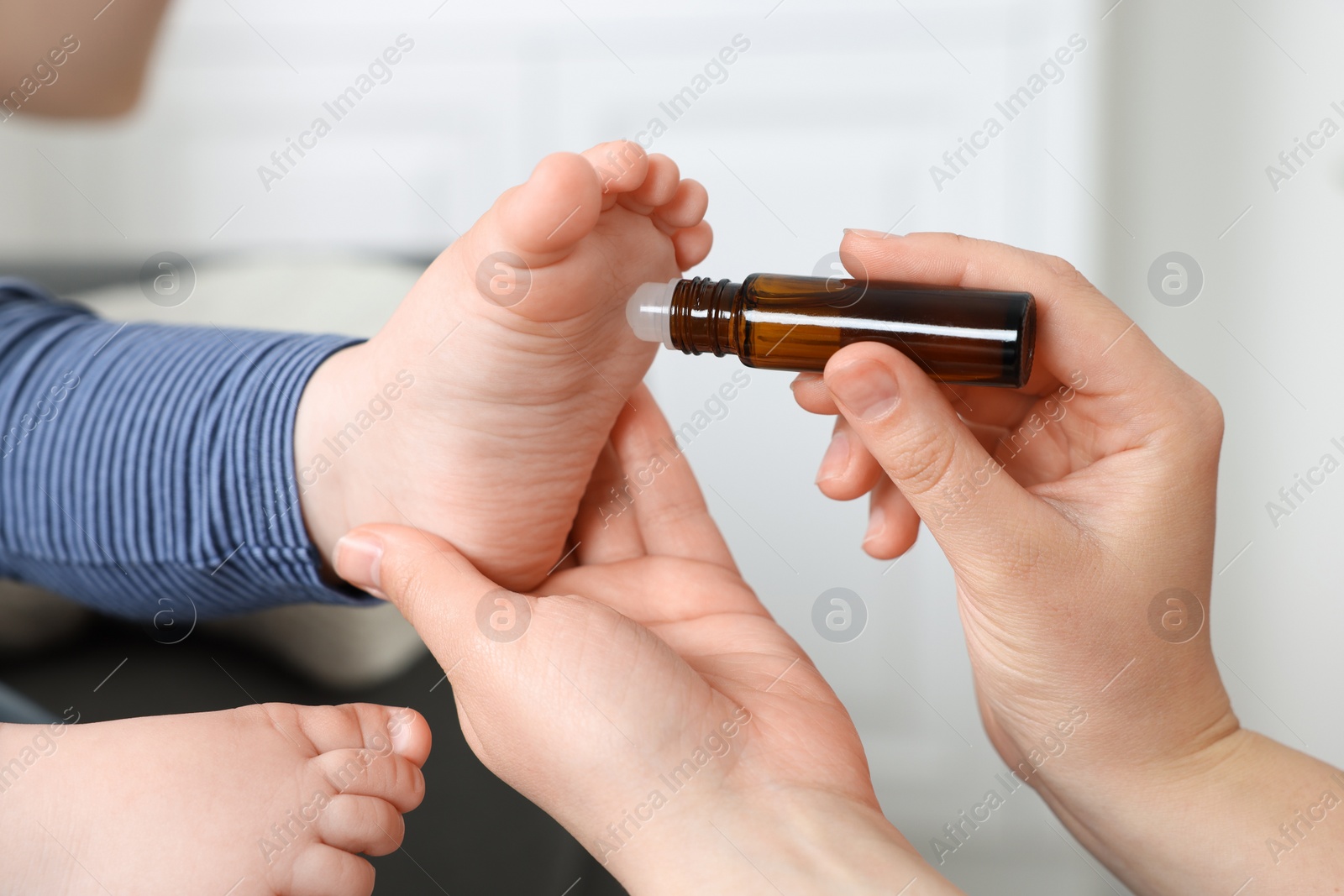 Photo of Mother applying essential oil from roller bottle onto her baby`s heel on blurred background, closeup