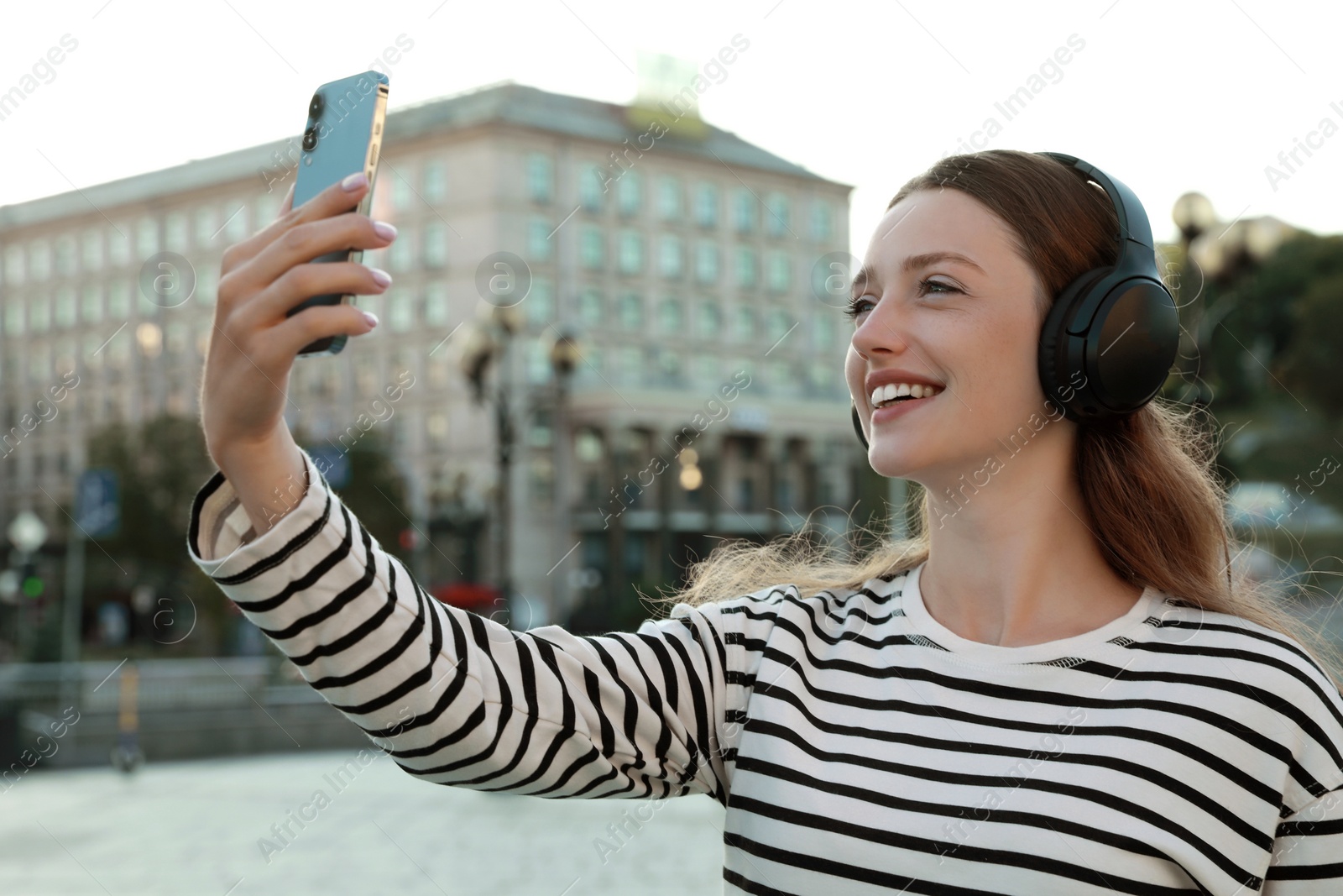 Photo of Smiling woman in headphones taking selfie on city street