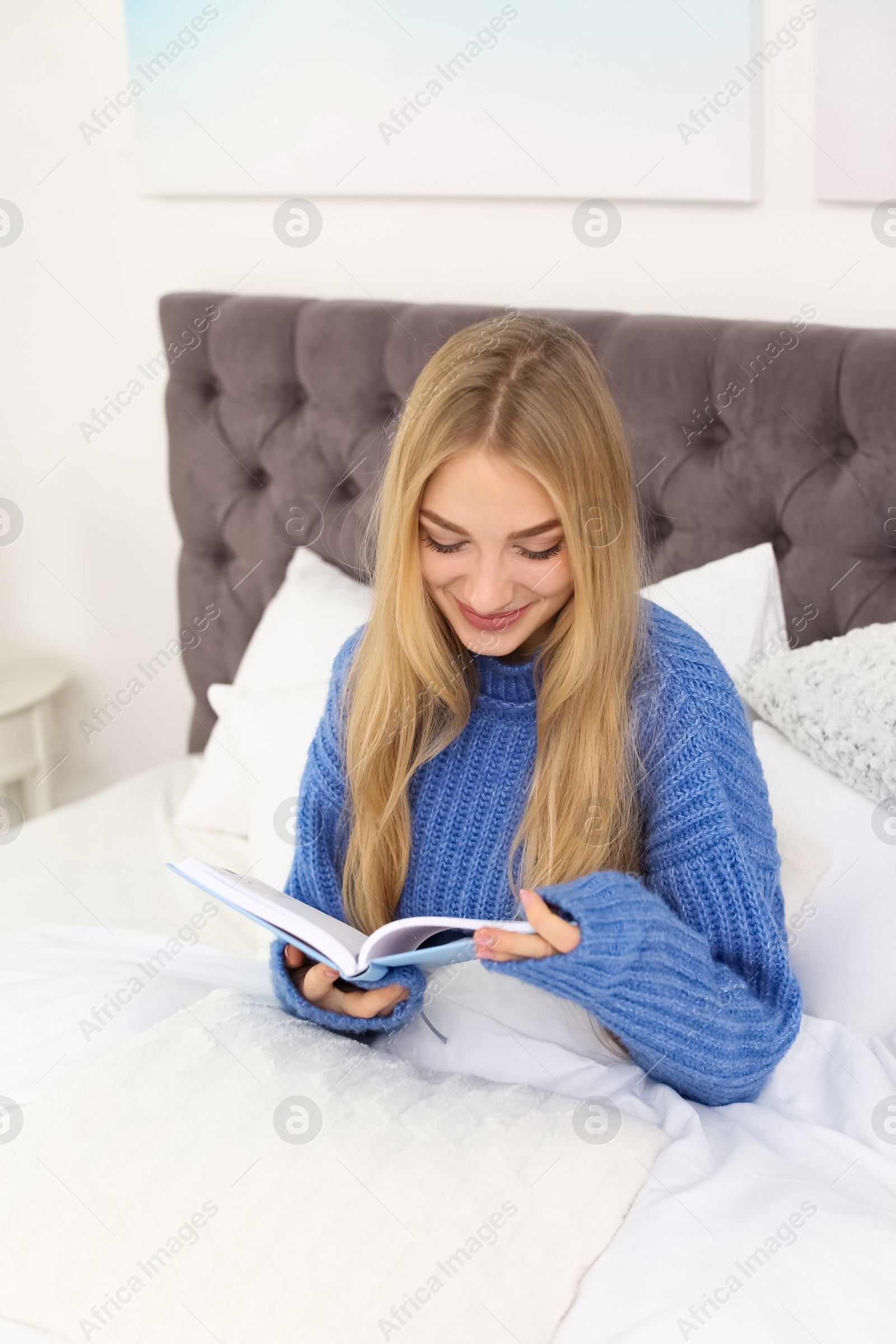 Photo of Beautiful young woman reading book in bed at home. Winter atmosphere