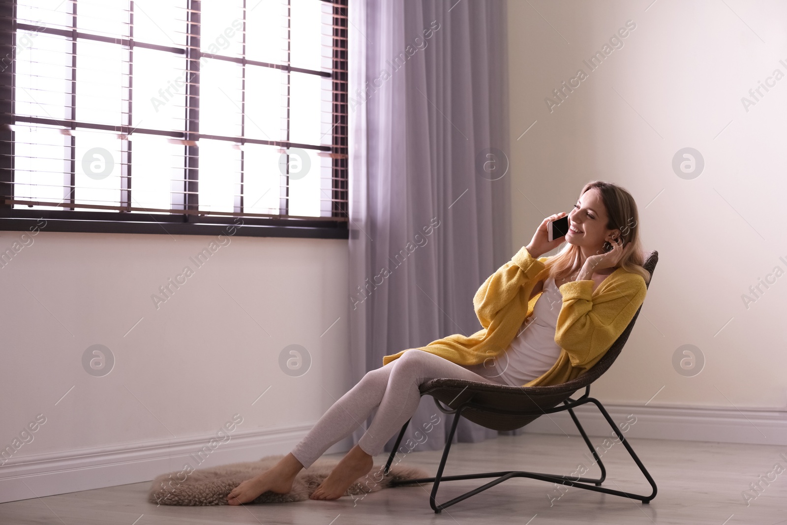 Photo of Young woman talking on phone near window with blinds at home. Space for text