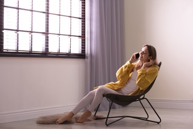 Photo of Young woman talking on phone near window with blinds at home. Space for text
