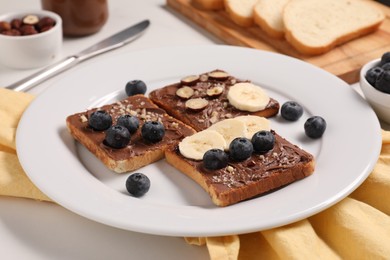 Photo of Toasts with tasty nut butter, banana slices, blueberries and hazelnuts on table, closeup