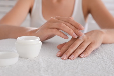 Woman applying cream onto hand on white towel, closeup