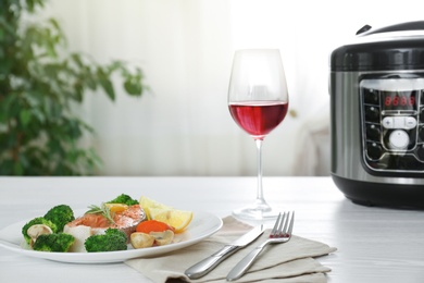 Photo of Plate with salmon steak and garnish prepared in multi cooker on table