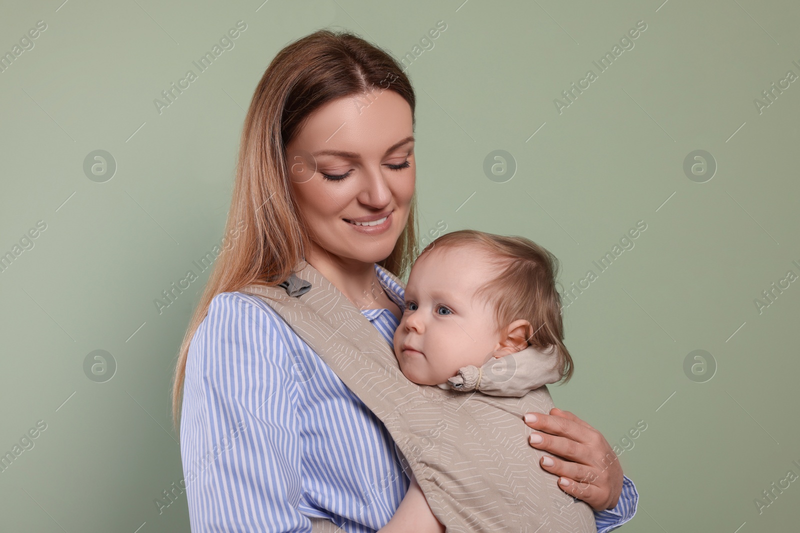 Photo of Mother holding her child in sling (baby carrier) on olive background