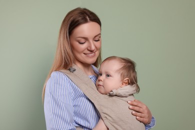 Photo of Mother holding her child in sling (baby carrier) on olive background