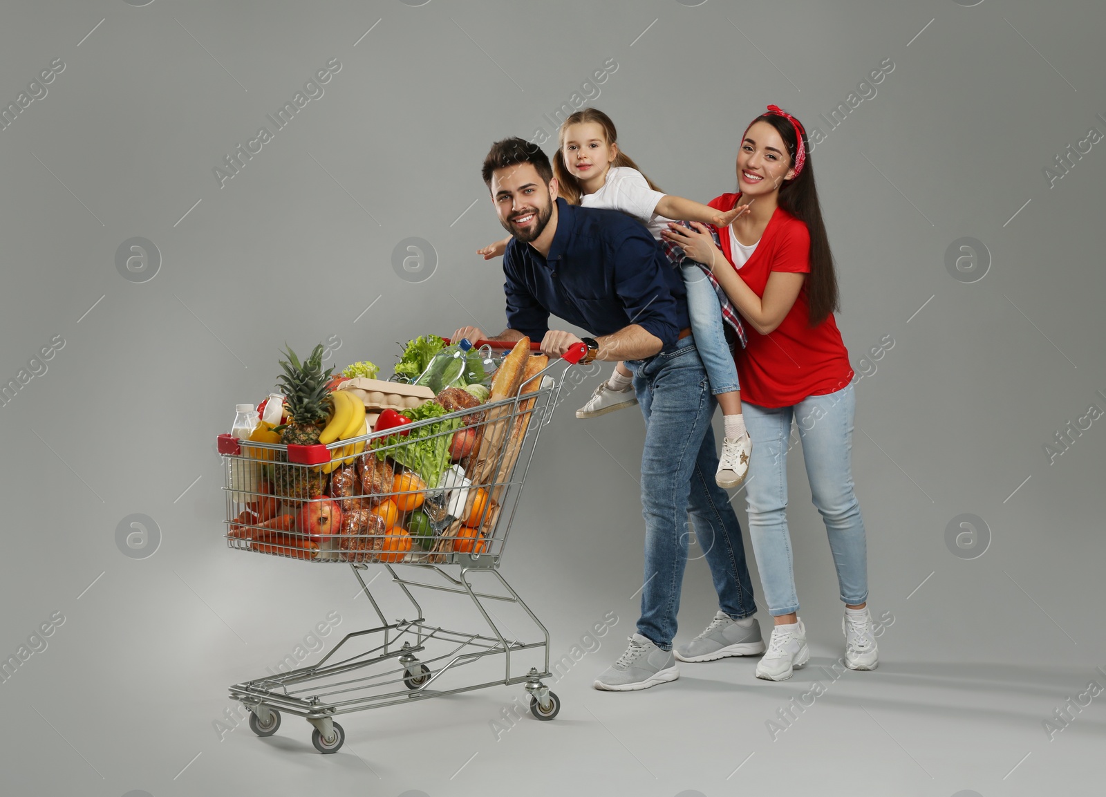 Photo of Happy family with shopping cart full of groceries on grey background