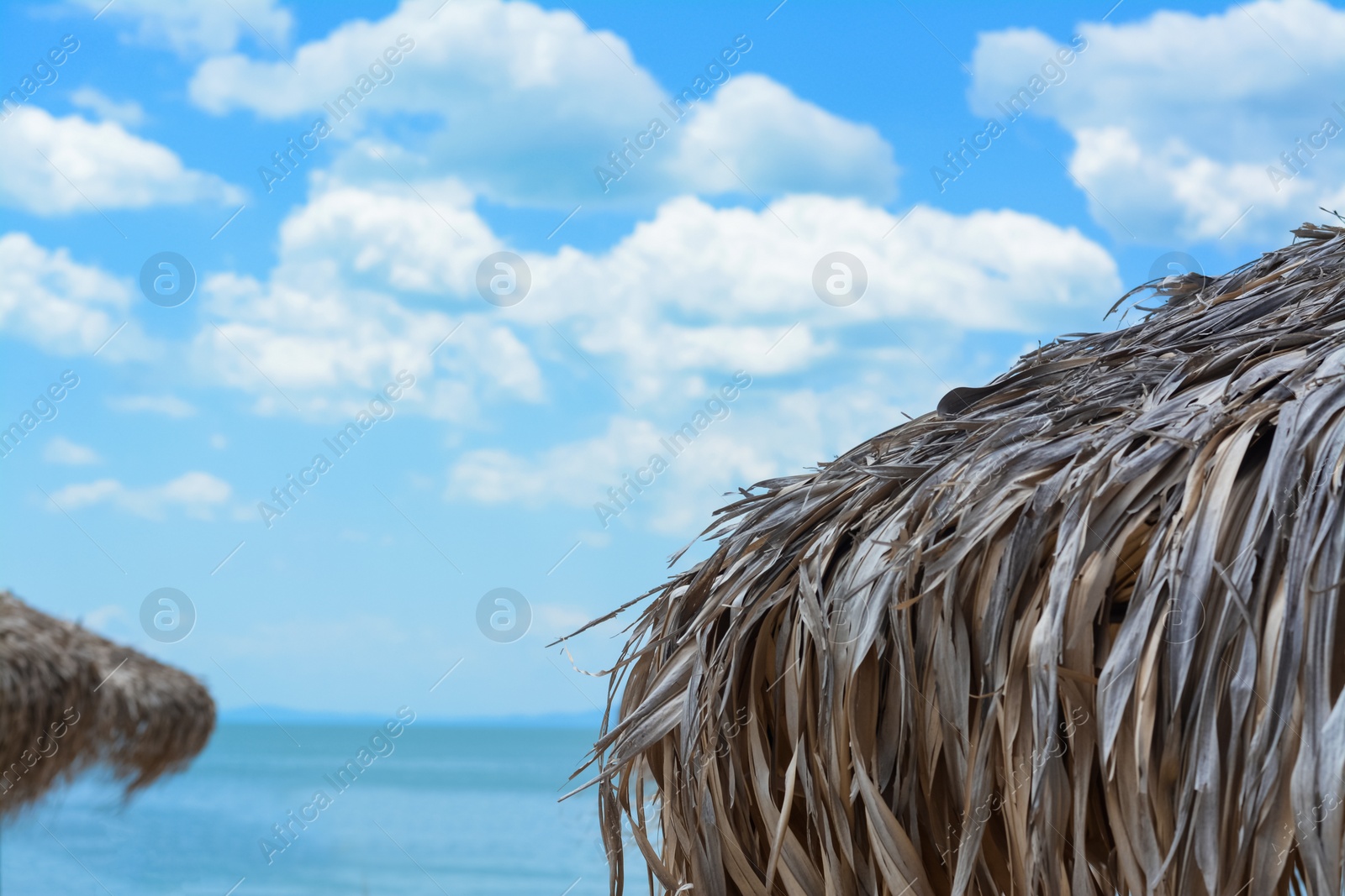 Photo of Beautiful straw beach umbrella against blue sky, closeup