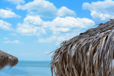 Photo of Beautiful straw beach umbrella against blue sky, closeup