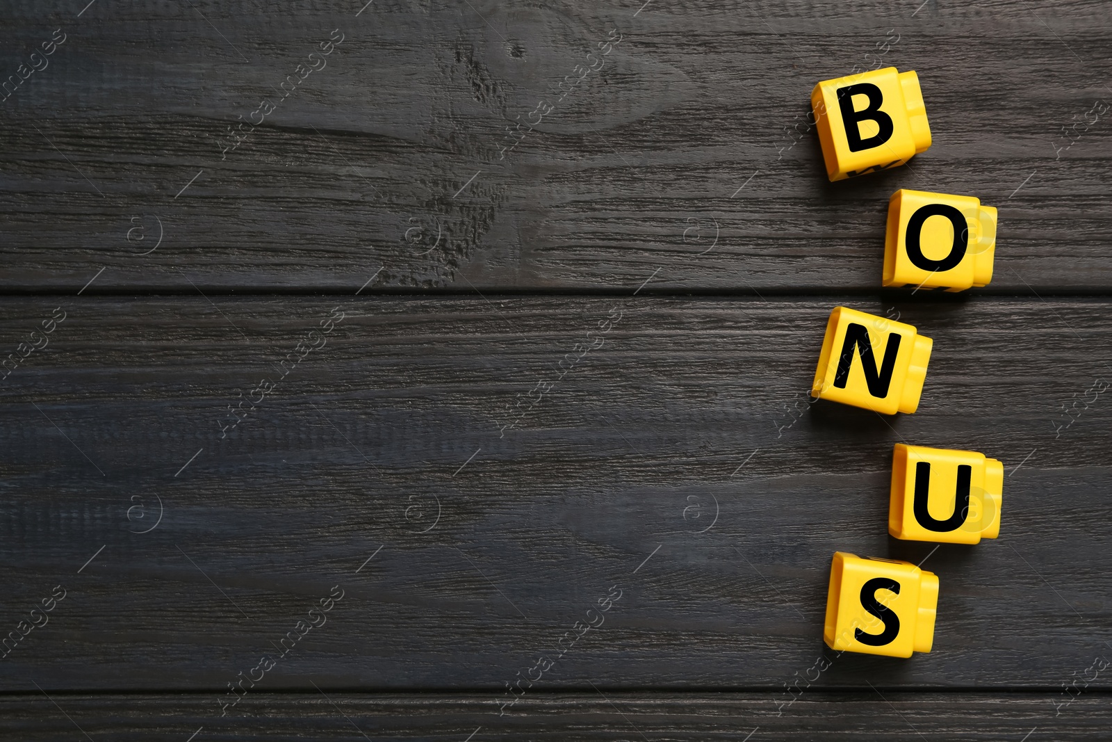 Image of Word Bonus made of yellow cubes with letters on wooden background, top view. Space for text