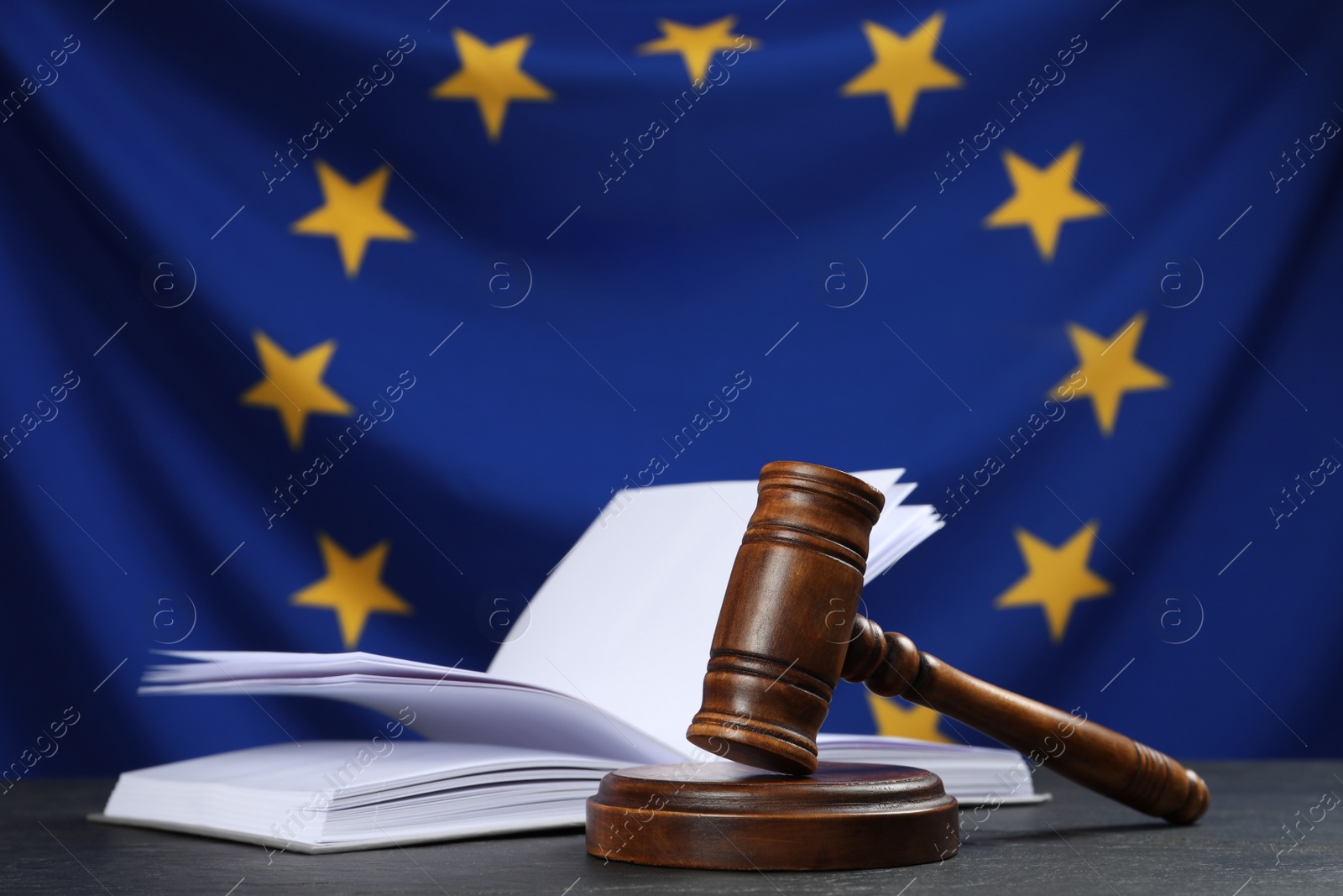 Photo of Judge's gavel and open book on black table against flag of European Union