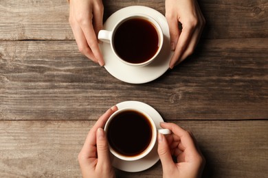 Photo of Women with cups of aromatic coffee at wooden table, top view