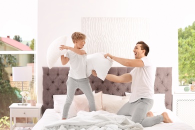 Photo of Father and son having pillow fight on bed at home