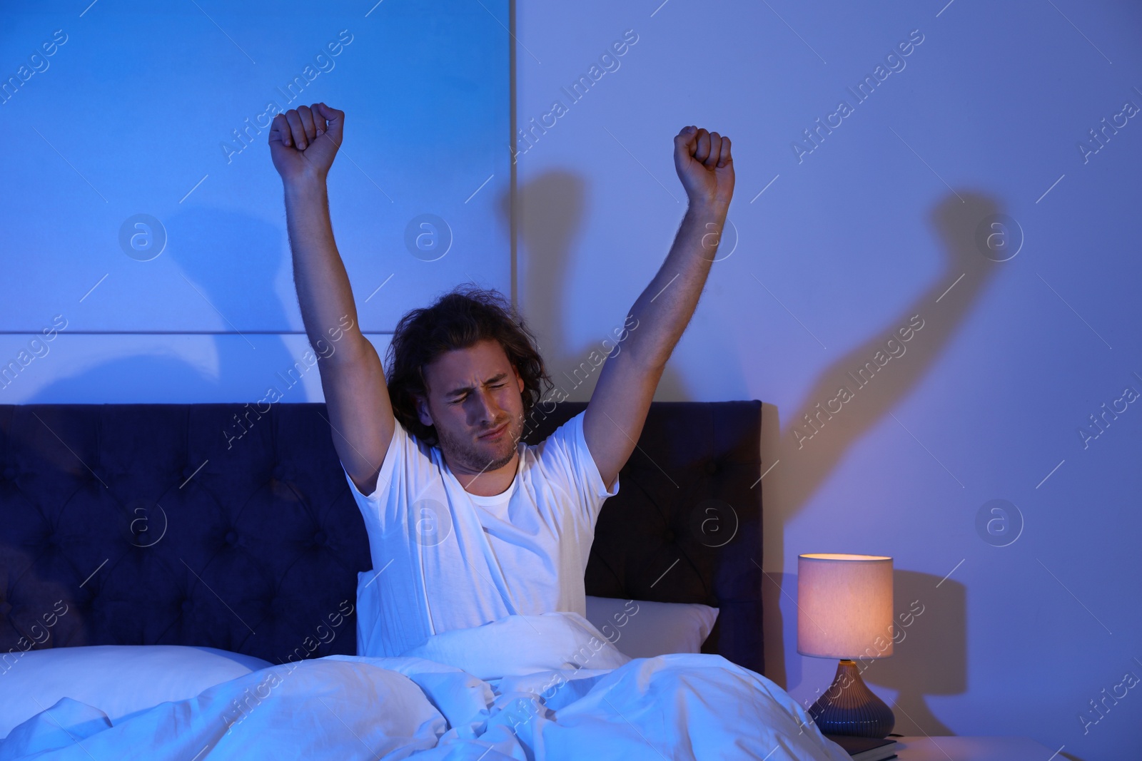 Photo of Sleepy young man stretching in dark room at night. Bedtime