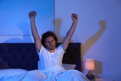 Photo of Sleepy young man stretching in dark room at night. Bedtime