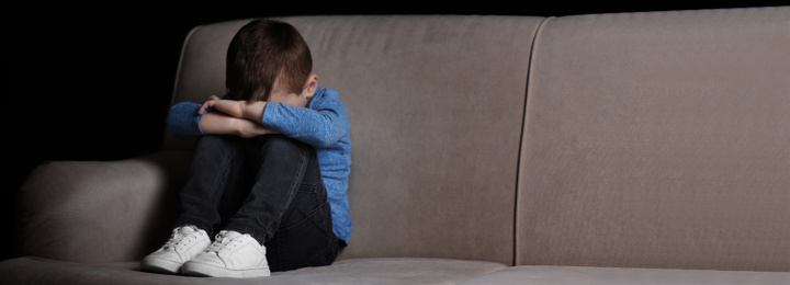 Image of Sad little boy sitting on couch at home, banner design with space for text. Time to visit child psychologist