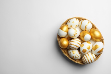 Wicker basket of traditional Easter eggs decorated with golden paint on white background, top view. Space for text