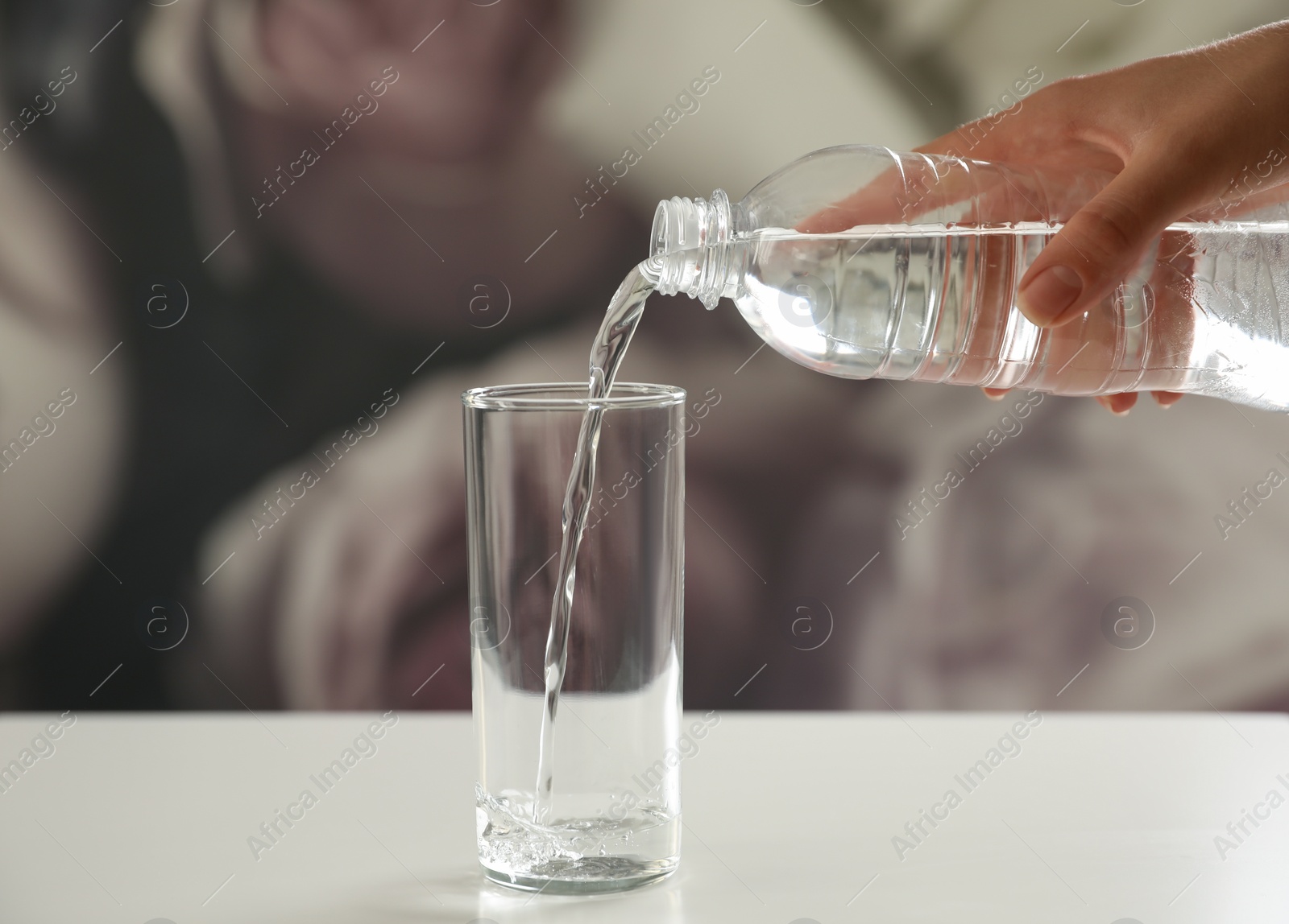 Photo of Woman pouring water from bottle into glass on table against blurred background, closeup