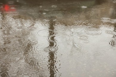 Photo of Rain drops falling down onto puddle outdoors